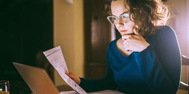 Young lady staring at laptop holding paper
