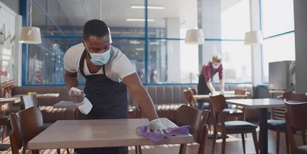 Man wearing medical mask cleaning table